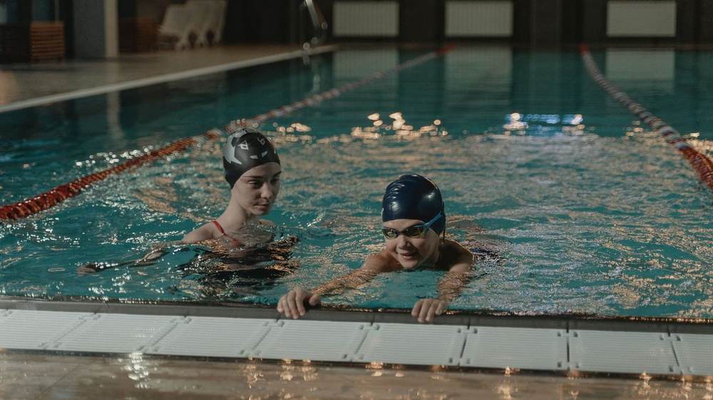 Two adults resting at the wall of an indoor lane pool during a lesson