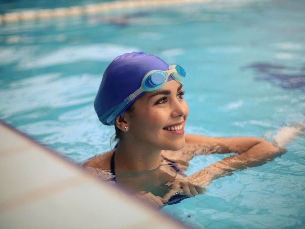 An adult swimmer in a cap, smiling at the pool edge